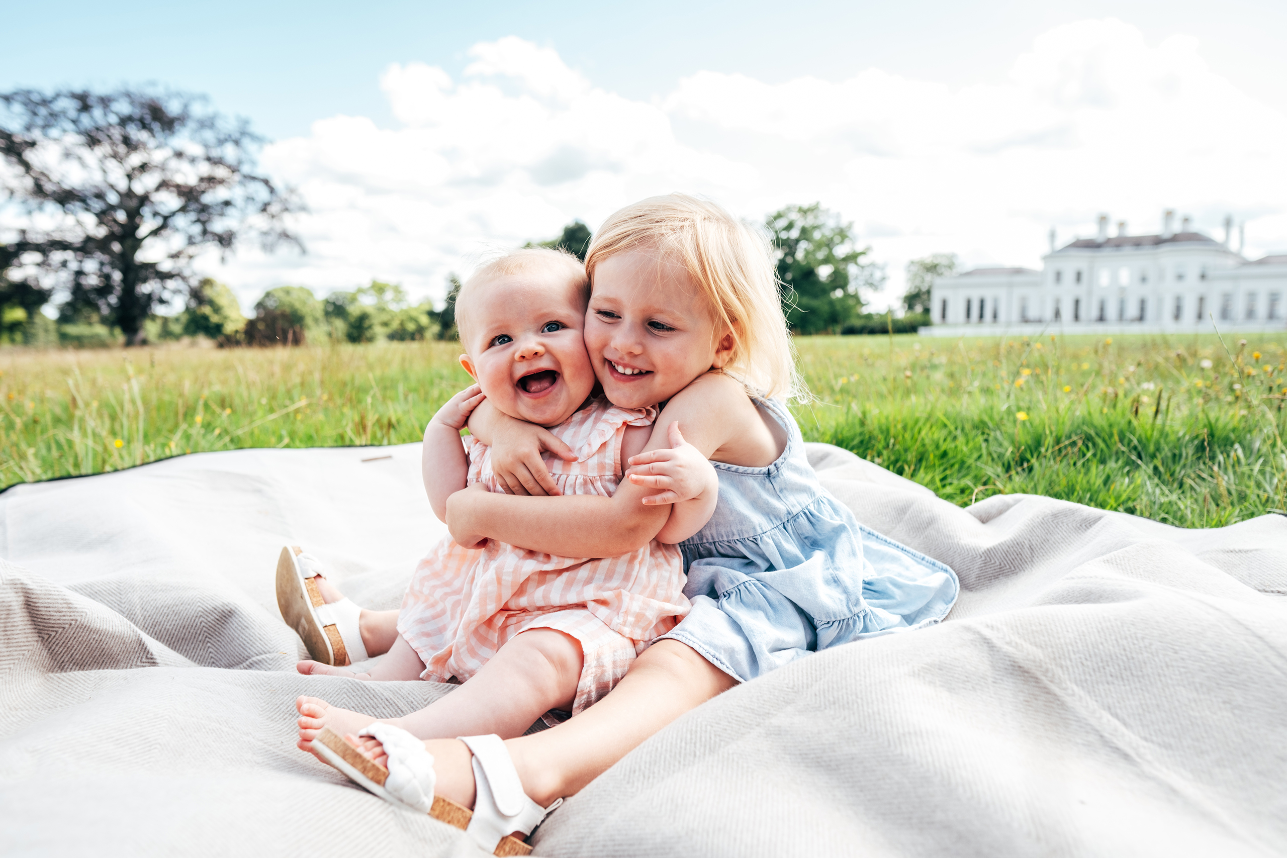 little girl hugs baby sister on blanket in front of Hylands House