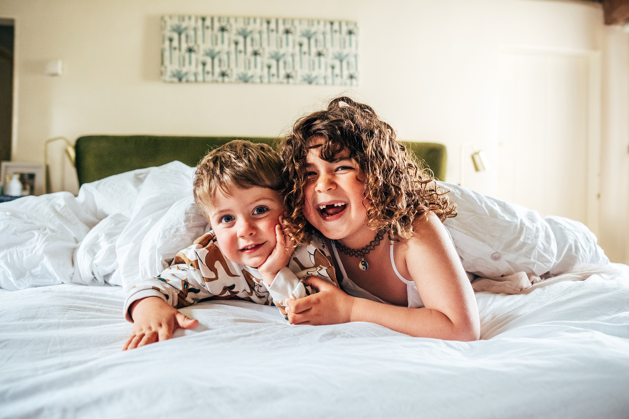 little girl with gappy grin hugs brother in pyjamas on bed