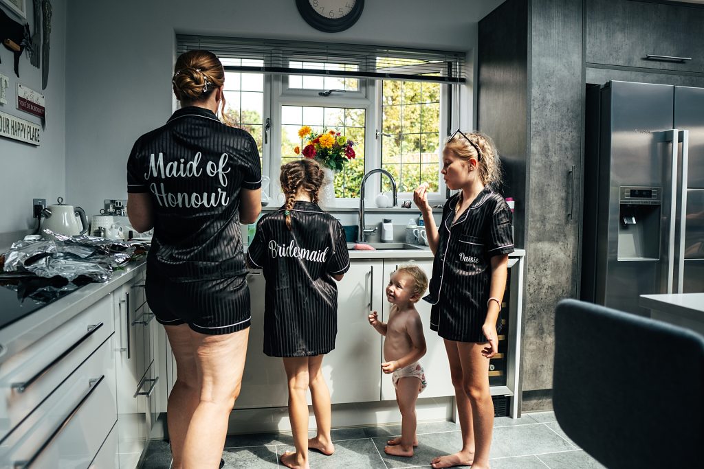 bridesmaids in black stripe pyjamas and baby in nappy eat snacks in a kitchen