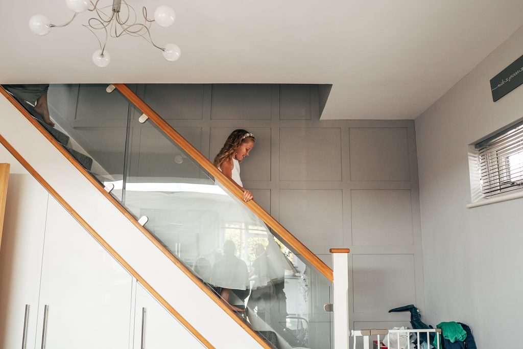 flower girl in white dress and flower crown comes down some stairs