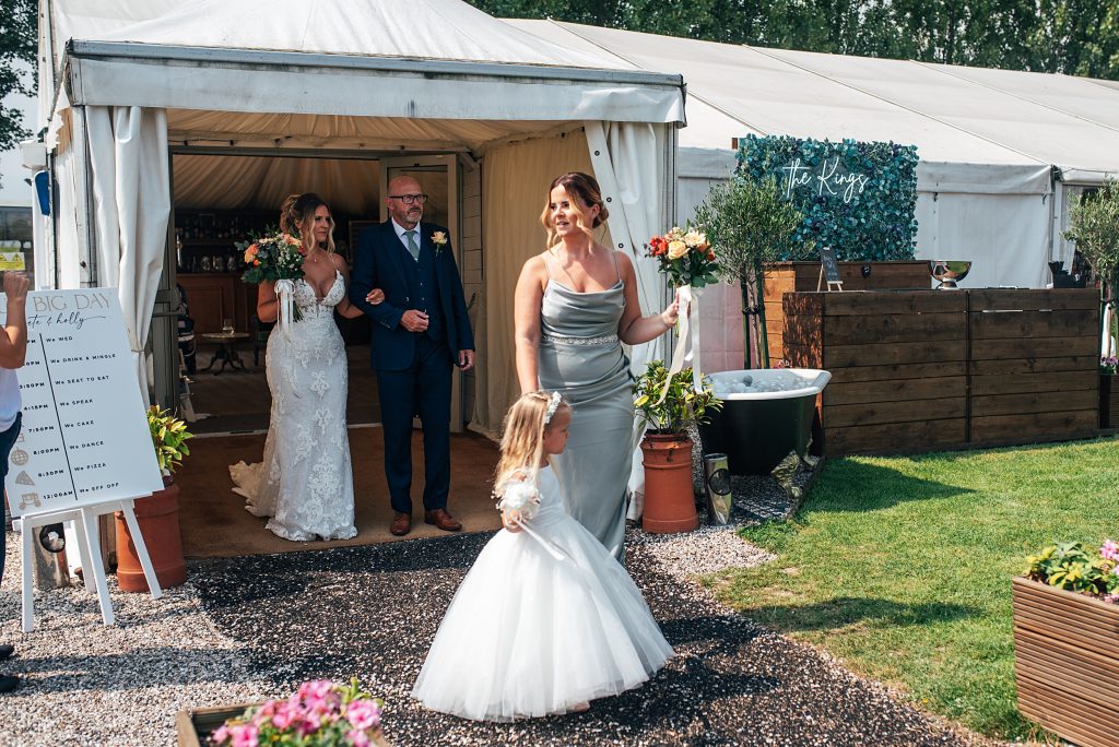 bridesmaid and flower girl ext a marquee with bride behind them