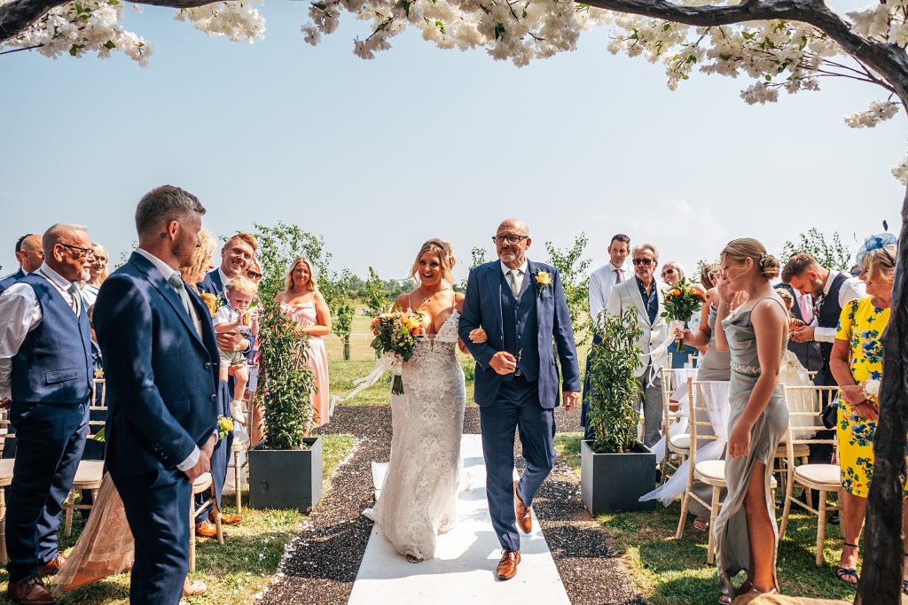 bride walks down aisle with her dad for outdoor ceremony
