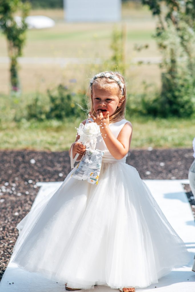 flower girl in white dress eats crisps