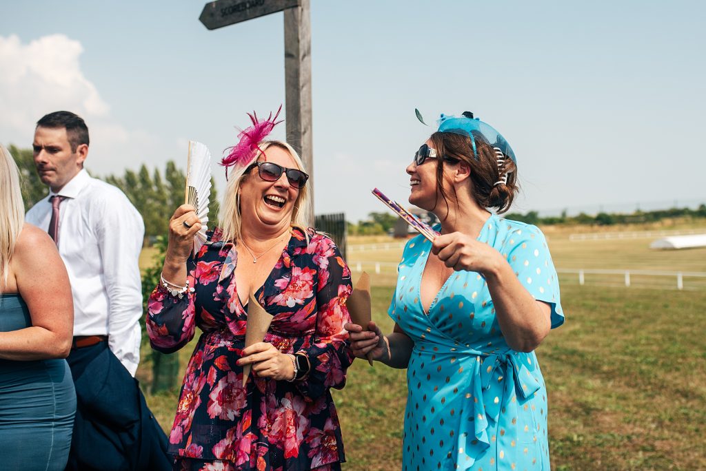 two laughing wedding guests fan themselves