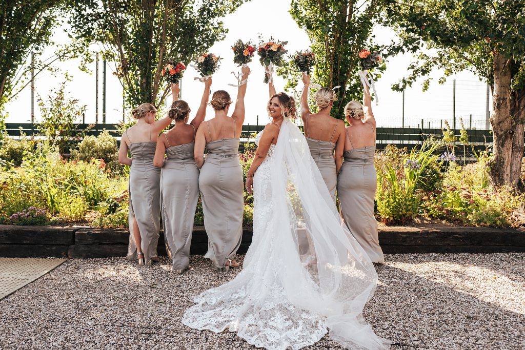 bride and bridesmaids with back to camera lift bouquets in air