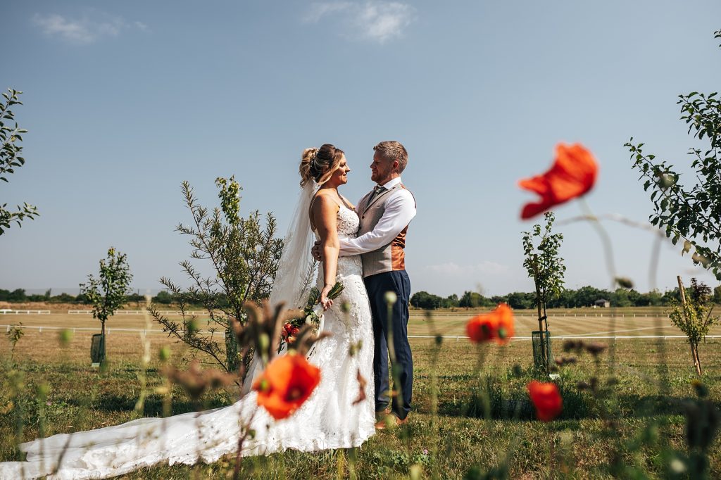 bride and groom stand together with poppies in foreground