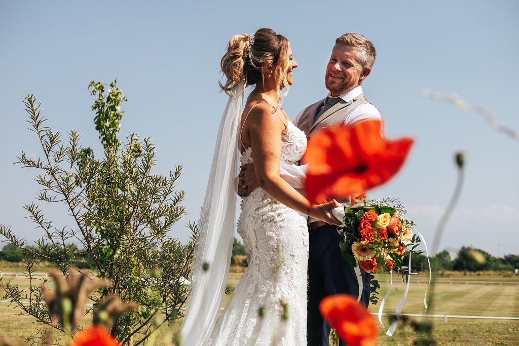 bride and groom laugh with poppies in foreground