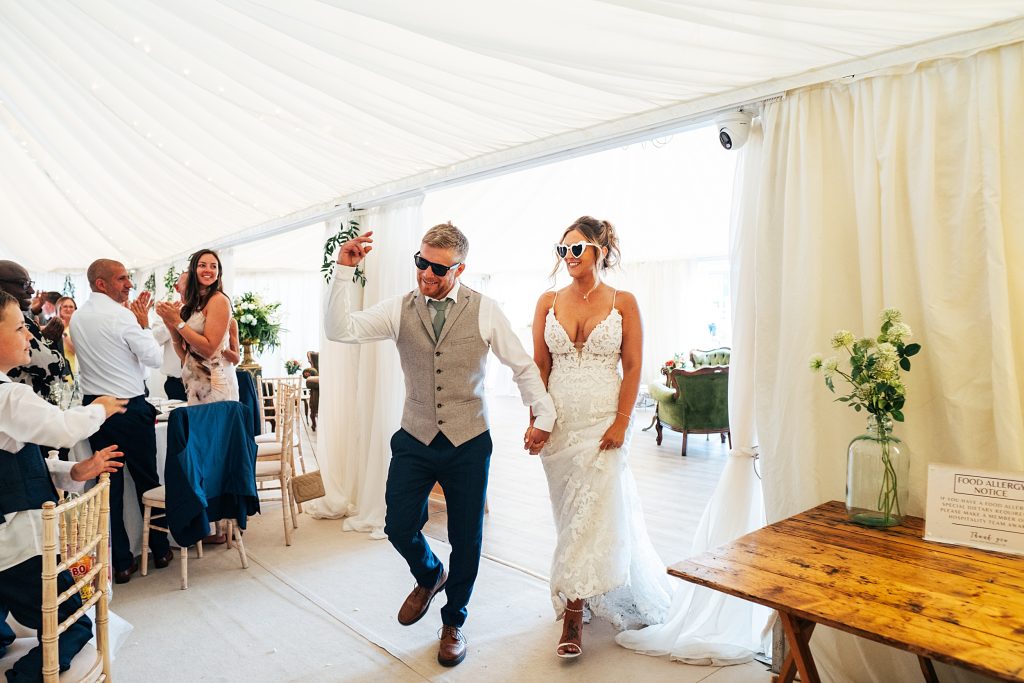 bride and groom wearing sunglasses enter reception in marquee