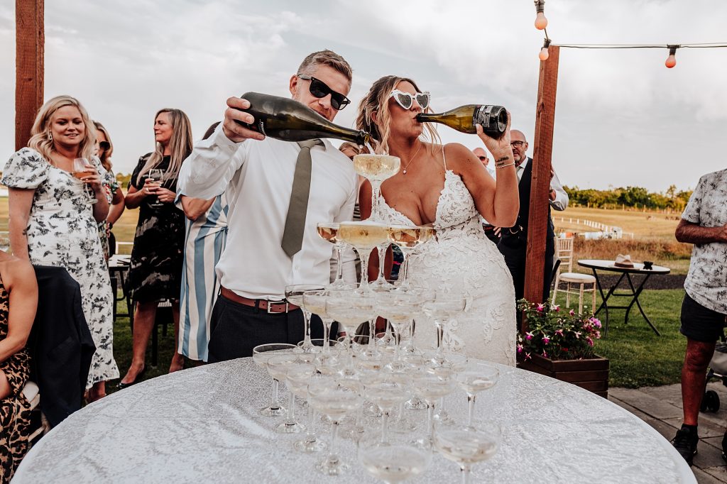 bride and groom in sunglasses pour champagne tower and swig from a bottle