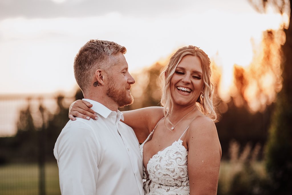 bride and groom laugh in field at sunset