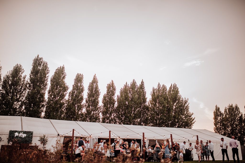 wide shot of wedding guests outside marquee on summer evening during sunset